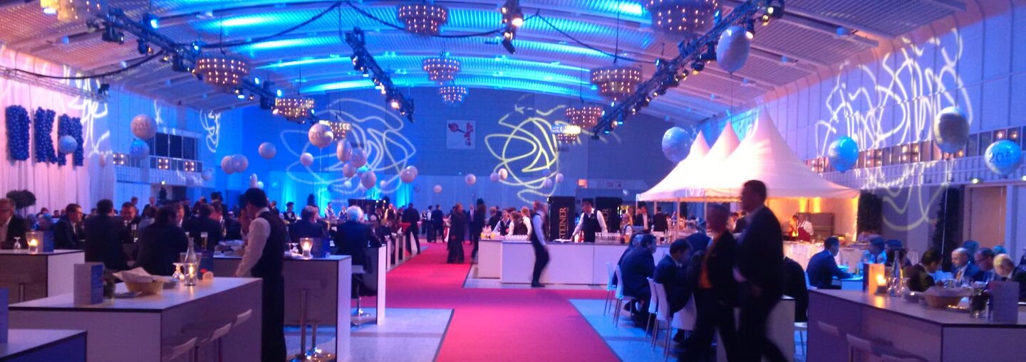 Get-together in Halle 1 mit Stehtischen, Tanzfläche und atmosphärischer Beleuchtung.