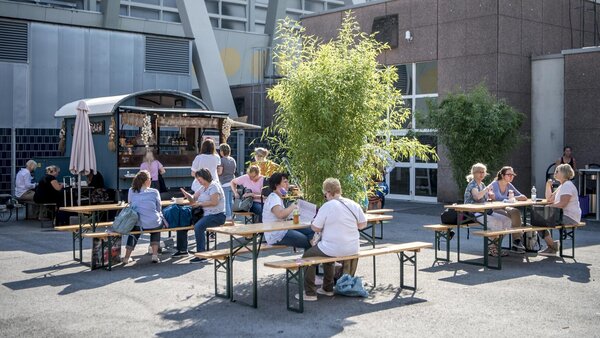 Innenhof der Messe Dortmund mit Foodständen, Bierzeltgarnituren und grüner Bepflanzung